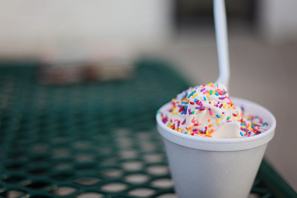 Ice cream in a cup with sprinkles and a spoon.